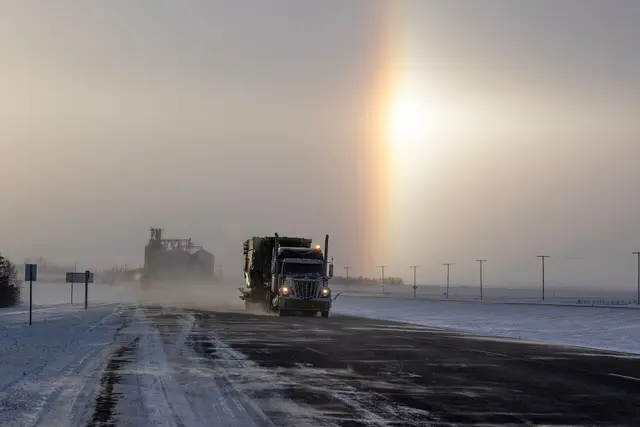 Truck on snowy highway with grain elevator and sun dog